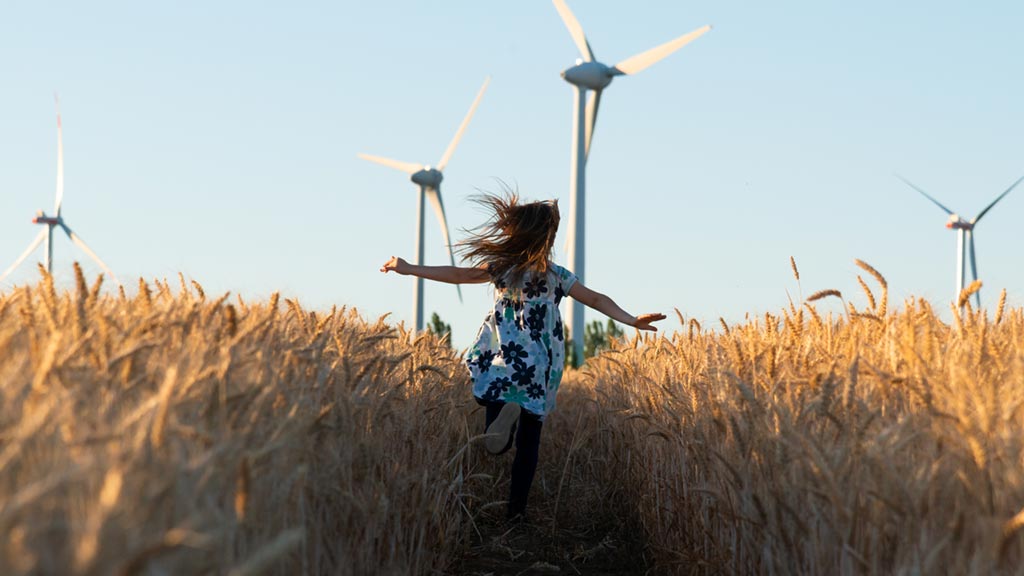 girl running on field with wind power turbine in the background